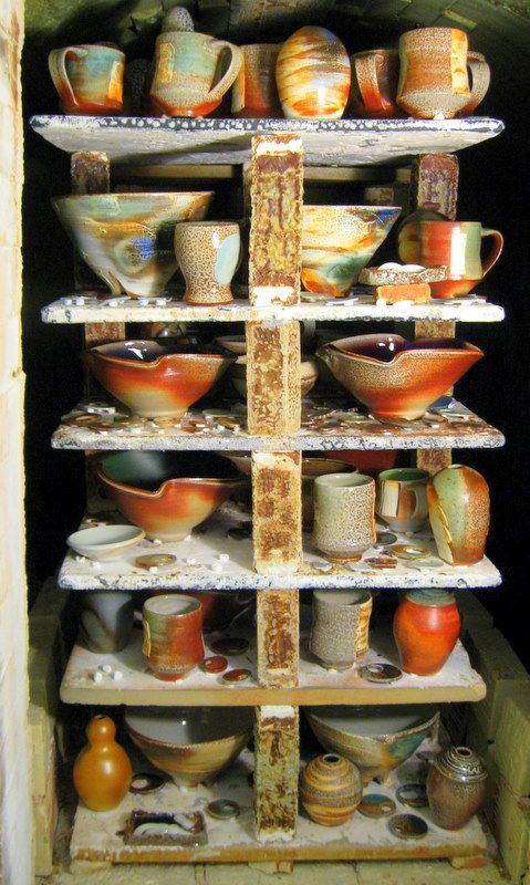 Rows of bowls, jars, cups, plates, and vessels still on the kilns racks.