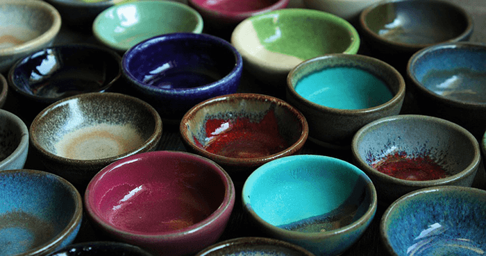Glazed teacups in an assortment of colors all lined up in rows to create a pattern.