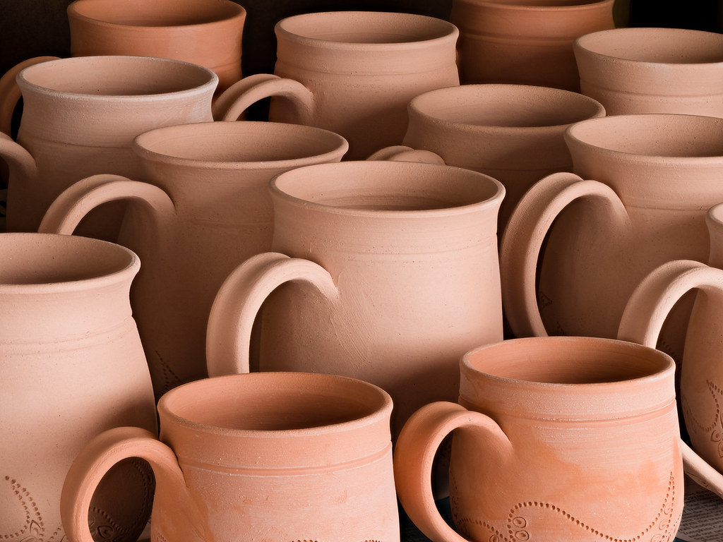 A sideways shot of terracotta colored bisqueware cups.